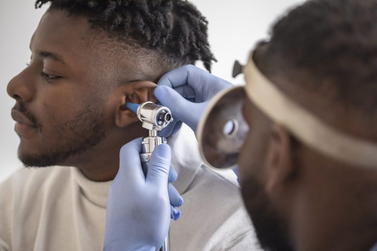 Close up of a male doctor carefully holding the ear of his patient to establish a clearer view of the inside of his ear, to see if he requires hearing aids at a modern clinic